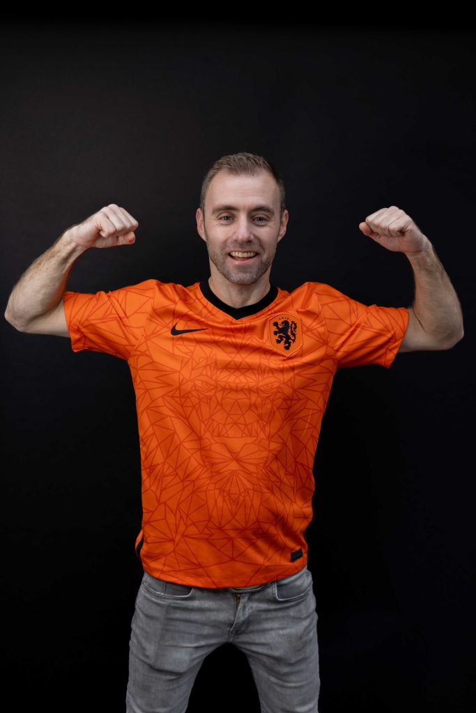 Dennis in een oranje voetbalshirt met beide armen in de lucht.