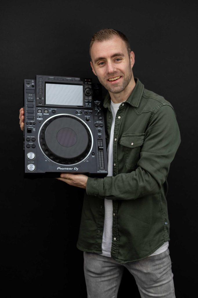 Dennis in een groen jasje met een DJ-speler op zijn schouder.