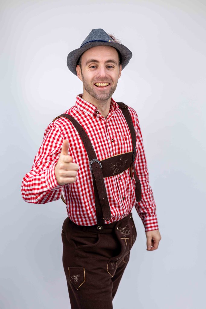 Dennis in après-ski-outfit met hoed en bretels steekt zijn duim op.