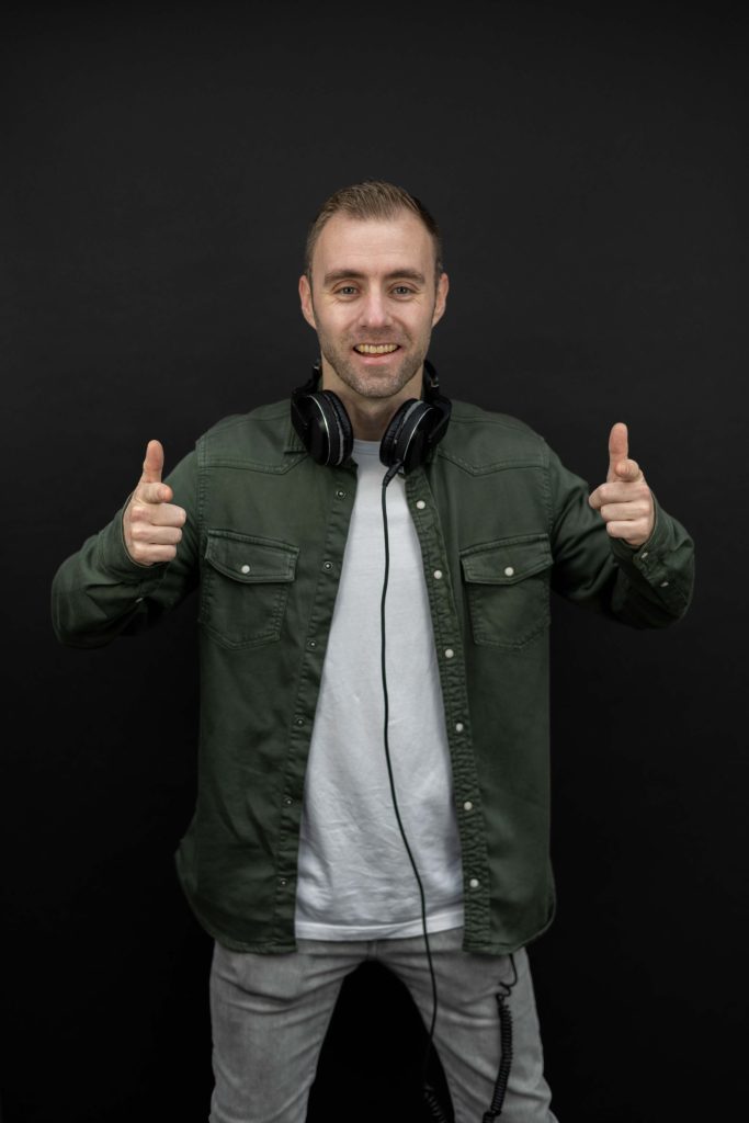 Dennis in een groen jasje houdt zijn koptelefoon bij één oor.
