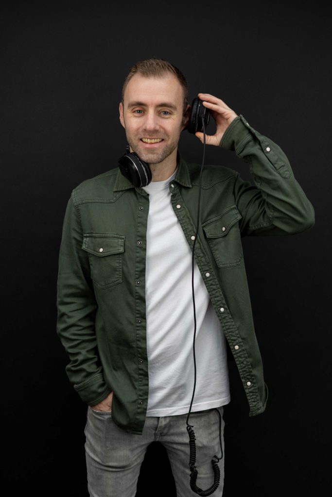 Dennis in een groen jasje met koptelefoon kijkt lachend naar beneden.