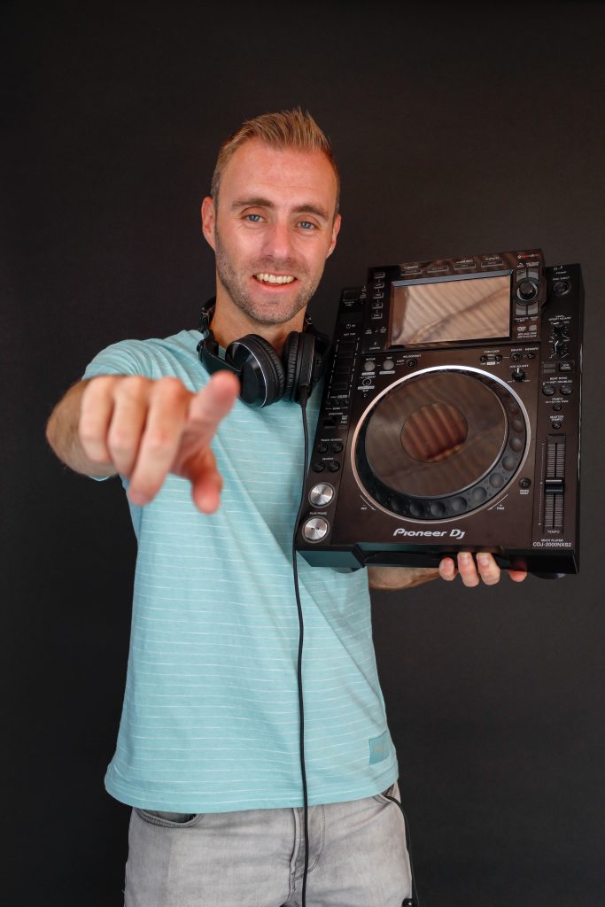 Dennis wijst naar de camera met een DJ-speler naast zijn gezicht.