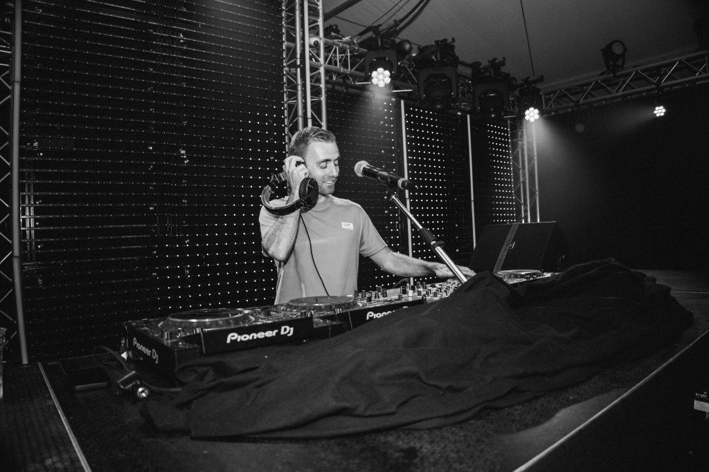 Zwart-witfoto van DJ Dennis met microfoon achter de draaitafel.