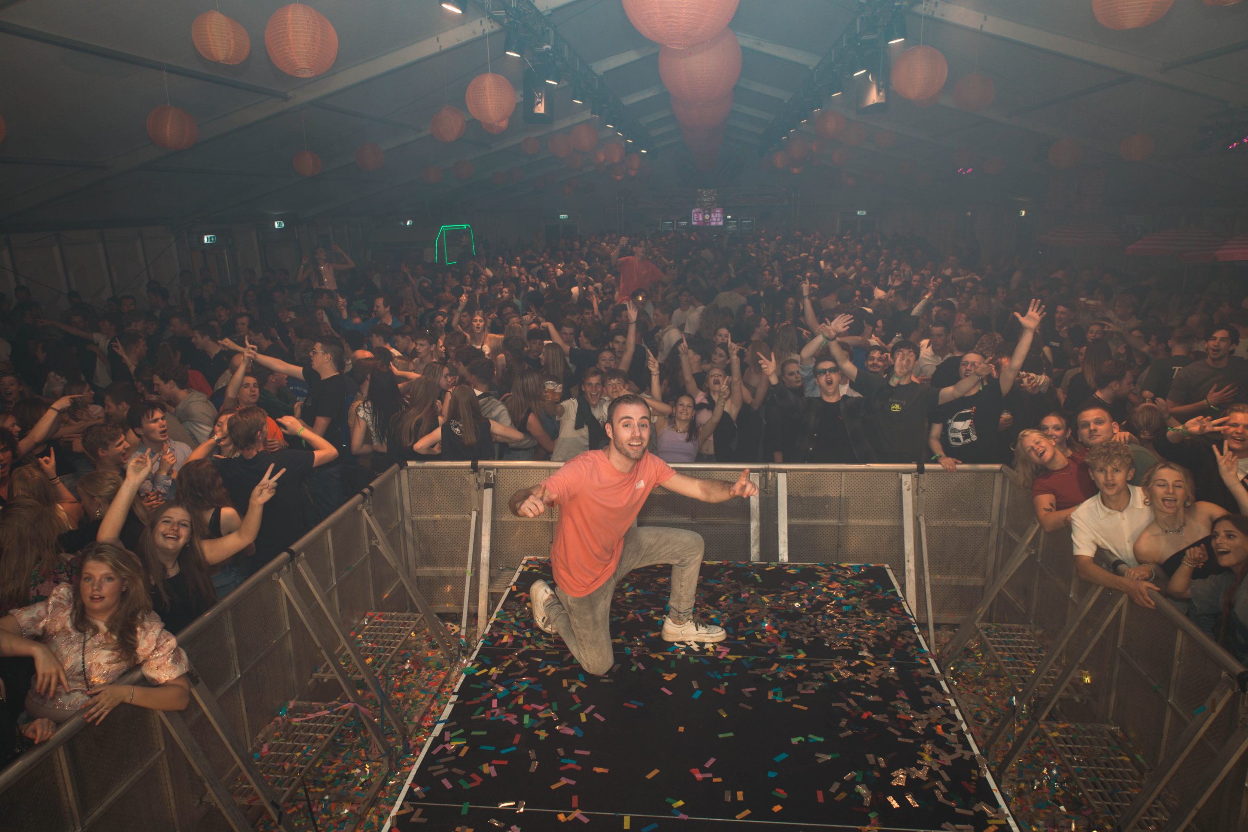 DJ Dennis bij de draaitafel voor een volle zaal met feestende gasten.