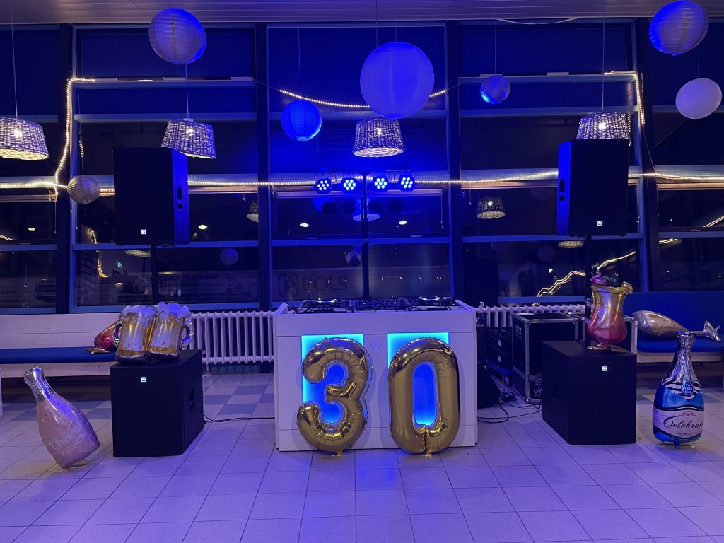 DJ-opstelling met blauwe verlichting en verlichte cijfers 30 in een feestzaal.
