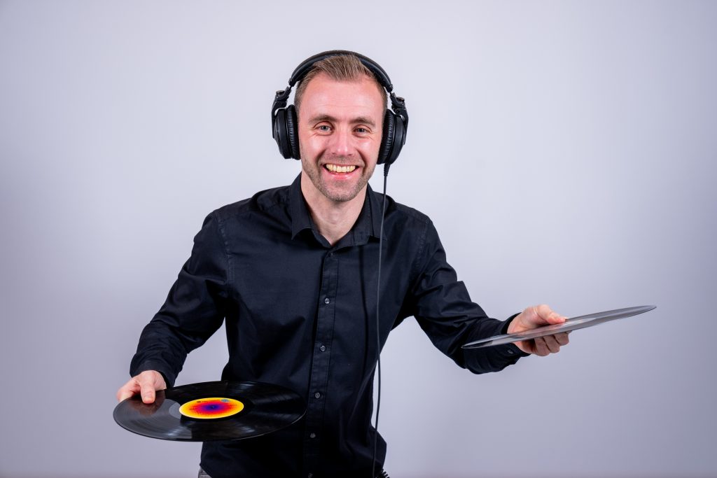 Dennis in een donker overhemd met koptelefoon en een drumstok in zijn hand.