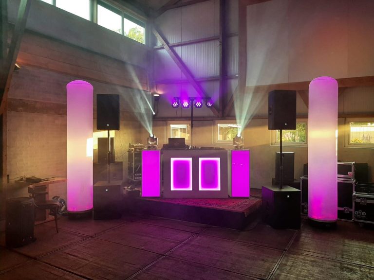Verlicht DJ-meubel met twee aircones, speakers en movingheads in een feestzaal.