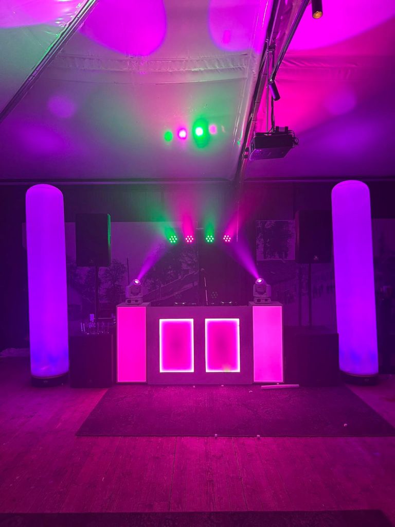 Roze verlichte DJ-opstelling met twee hoge aircones en movingheads in een feesttent.